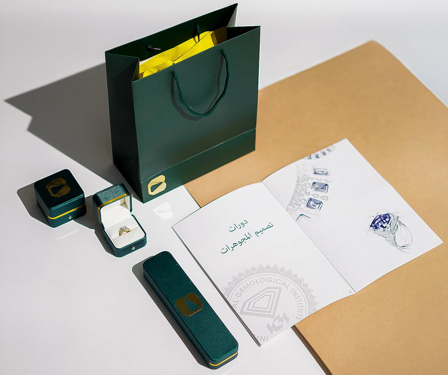 Luxury jewelry packaging featuring an open ring box with a 0.36 CT Dual Marquise Lab-Grown Diamond Ring, a green shopping bag, and an Arabic-labeled certificate/booklet on a beige surface.
