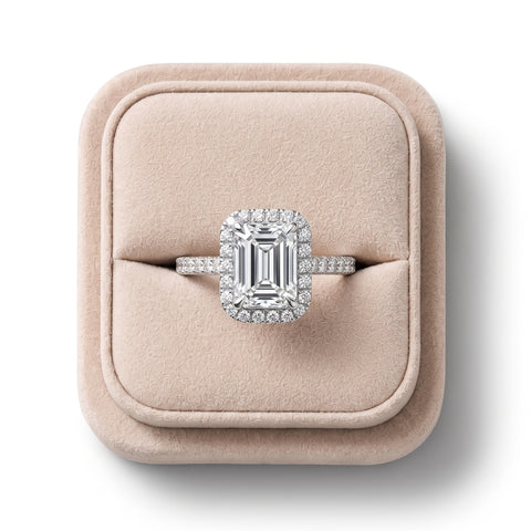 Emerald cut lab grown diamond ring with a round diamond halo, set in an 18K gold band, showcased on a soft display.