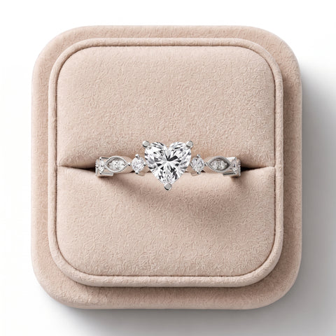 Heart-shaped lab diamond ring with round accent diamonds, milgrain detail, and a tapered band, displayed on a soft jewelry box.